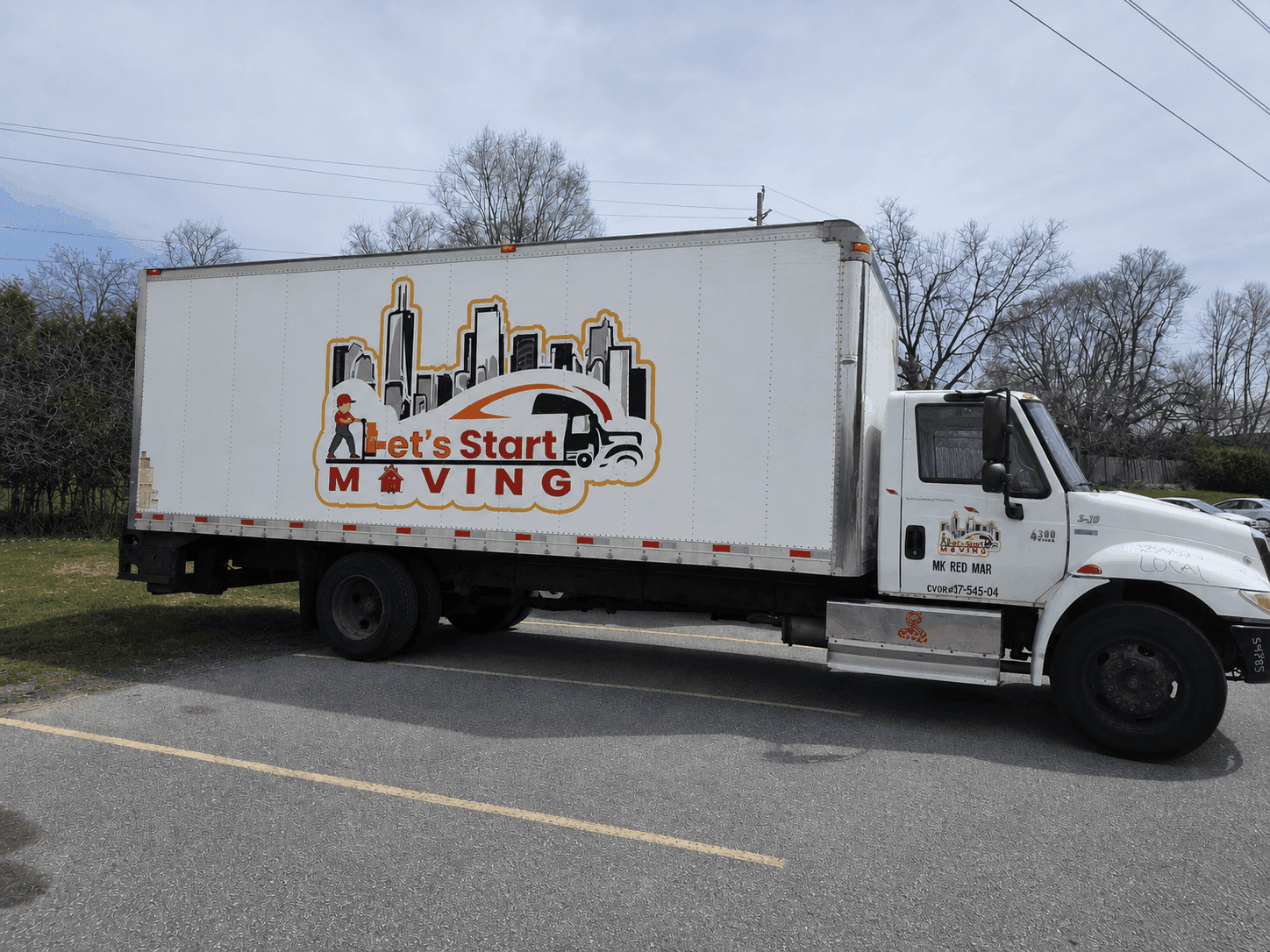 Side view of a white Let's Start Moving box truck with the company skyline logo, parked outdoors.